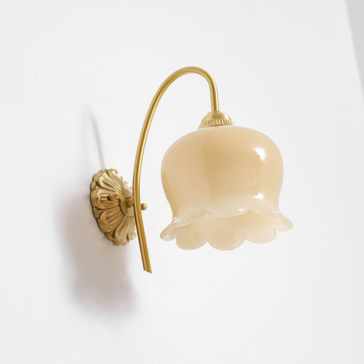 Angled view of the unlit Clérachic wall light, with the cream glass bell and ridged brass cap in clear detail.
