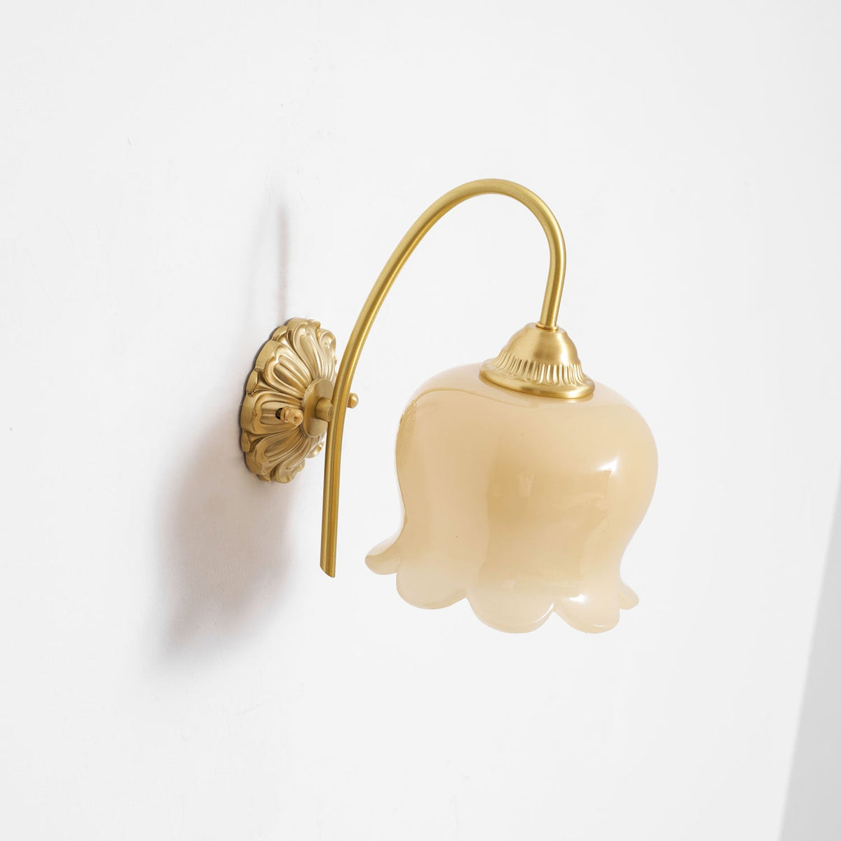 Clérachic wall light unlit, with its creamy glass shade and round brass back plate shown from the side.