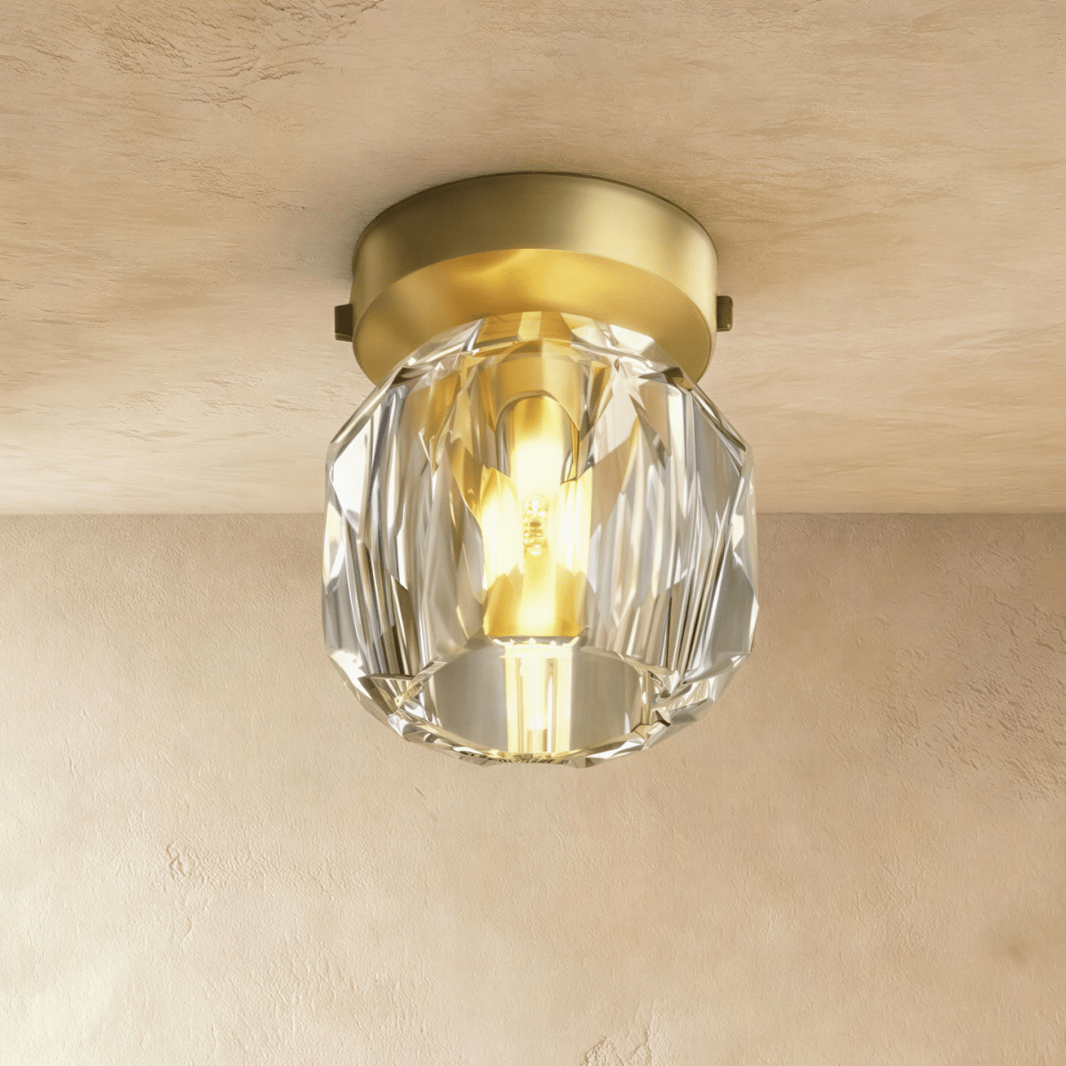 Clérachic ceiling light in close-up, a faceted crystal shade glowing around its bulb beneath a gold ceiling plate.