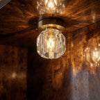 Close view of the Clérachic faceted crystal ceiling light glowing warm against a dark burr-wood alcove.