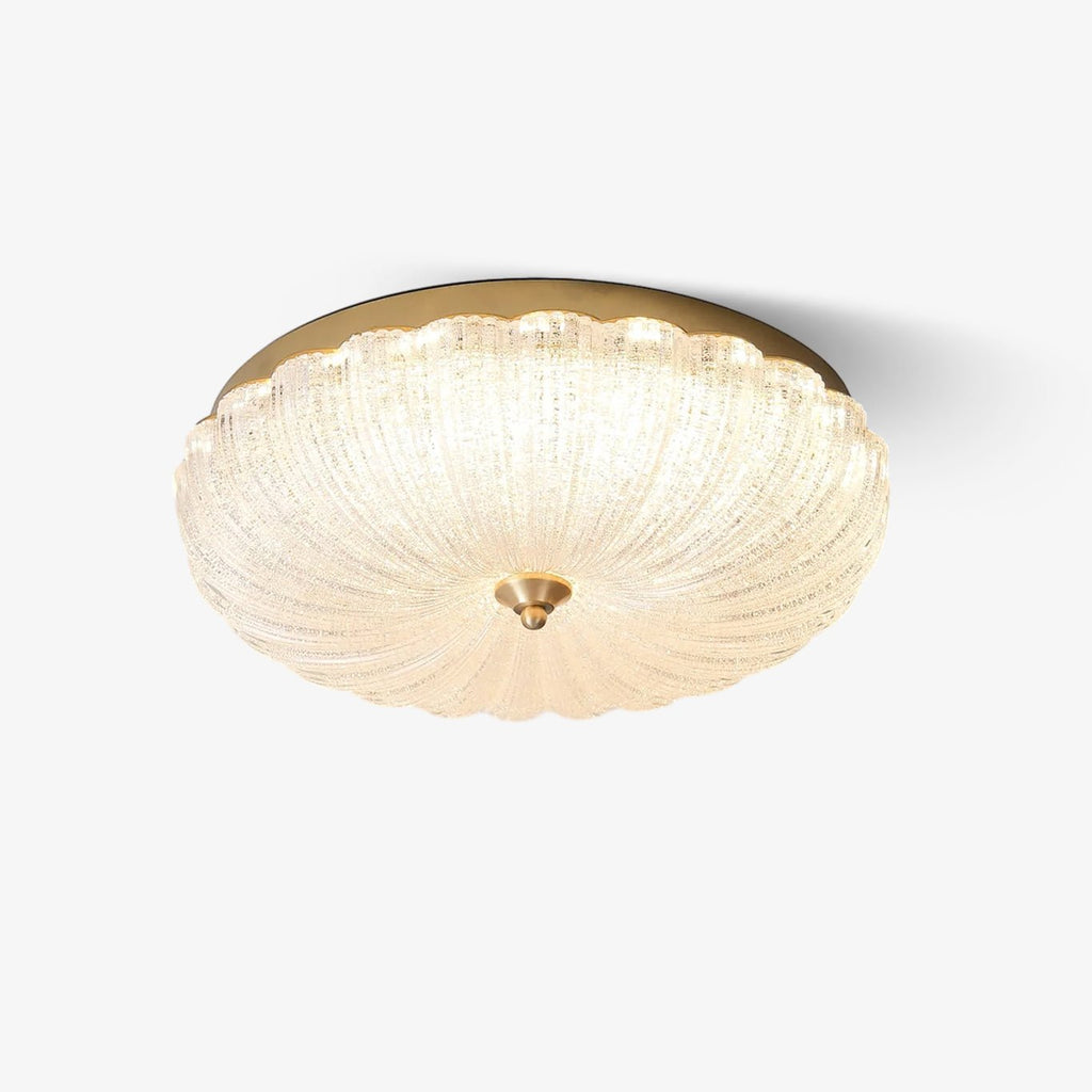 Scalloped, frosted glass flush-mount ceiling light with a gold edge and a small brass finial, lit on a plain white backdrop from Clérachic.
