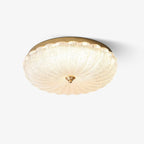 Scalloped, frosted glass flush-mount ceiling light with a gold edge and a small brass finial, lit on a plain white backdrop from Clérachic.