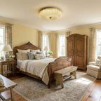 Lit Clérachic flush ceiling light with a ribbed glass shade over a bedroom with a carved wooden bed, a wardrobe and a patterned rug.