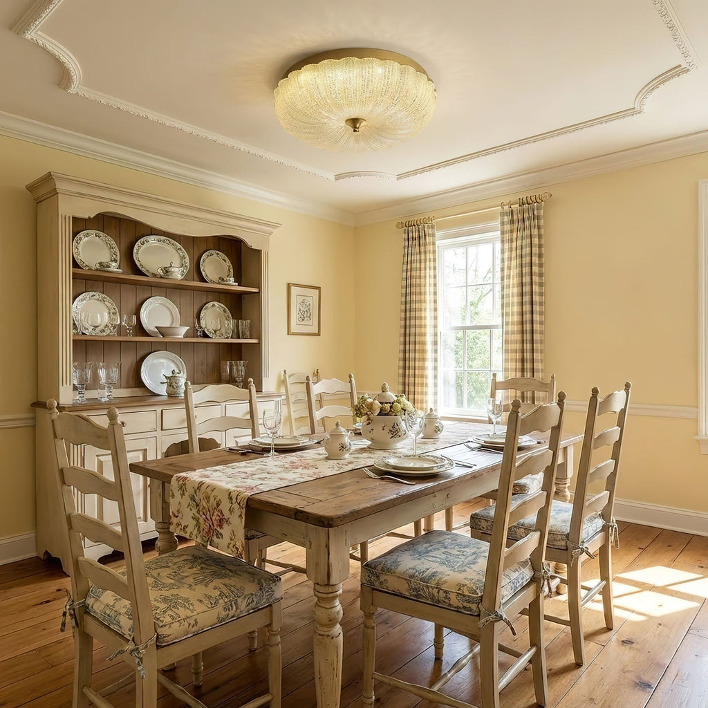 Glowing Clérachic glass ceiling light in a yellow dining room with a plate dresser, a wooden table and ladder-back chairs.