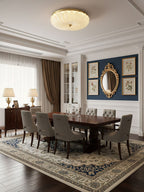 Clérachic ceiling light lit above a dark wood dining table with grey chairs, a navy wall with a gold mirror and table lamps beyond.