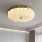 Low-angle view of the lit ribbed glass shade and gold rim of this Clérachic ceiling light, with a soft cove light along the wall.