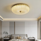 Clérachic ceiling light glowing above a calm bedroom with a cream headboard, panelled wall and a vase of branches on a bedside table.