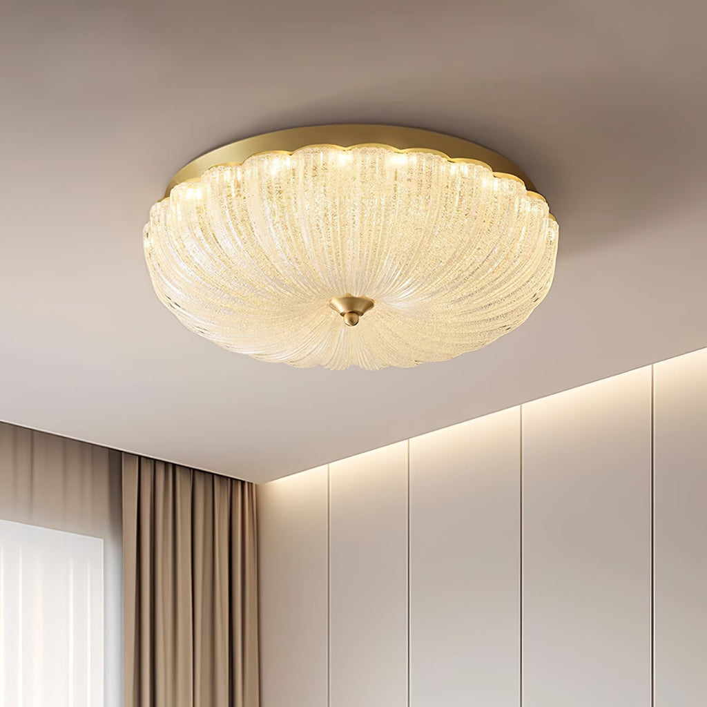 Close low view of the ribbed, sparkling glass shade and gold backplate of this Clérachic ceiling light beside a cove-lit wall.