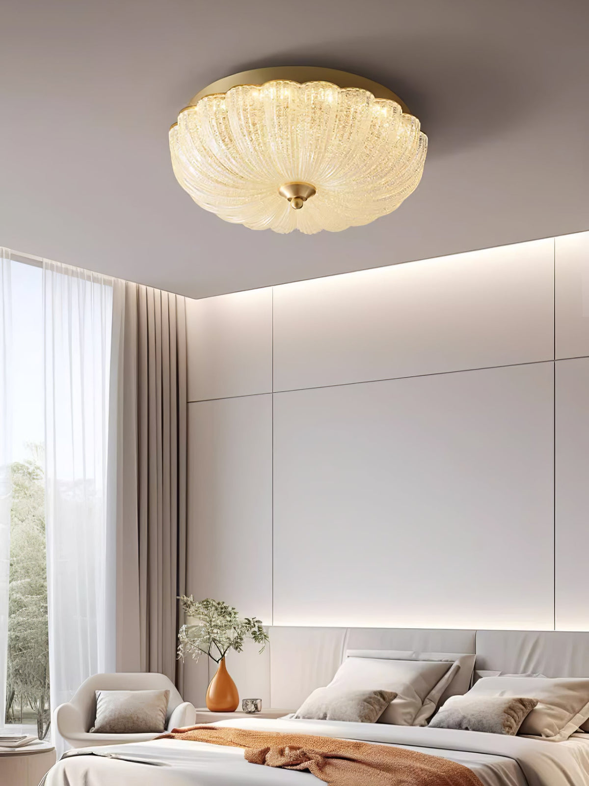 Clérachic ceiling light lit above a tall bedroom window with soft curtains, a bed with a rust throw and an armchair in the corner.