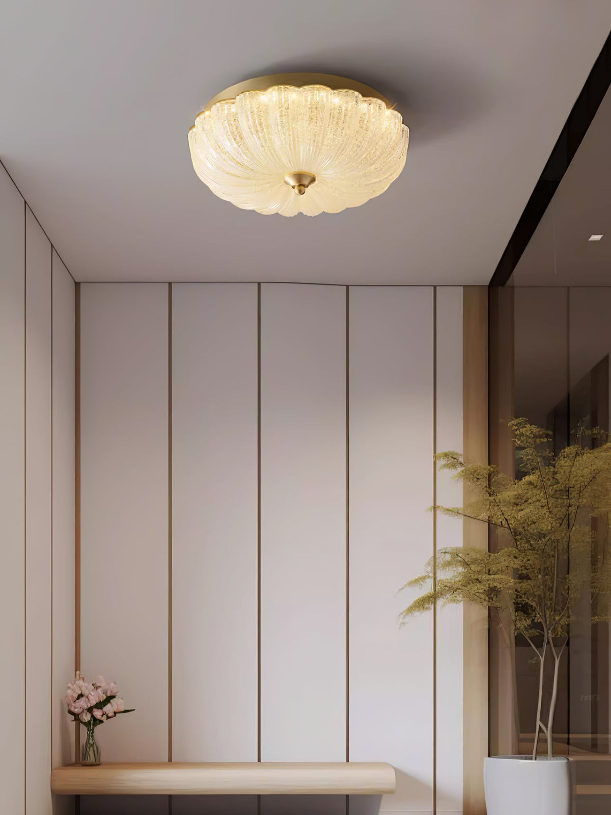 Clérachic ceiling light above a hallway with tall cream panels, a wooden bench, a pink bloom and a tall plant at the edge.