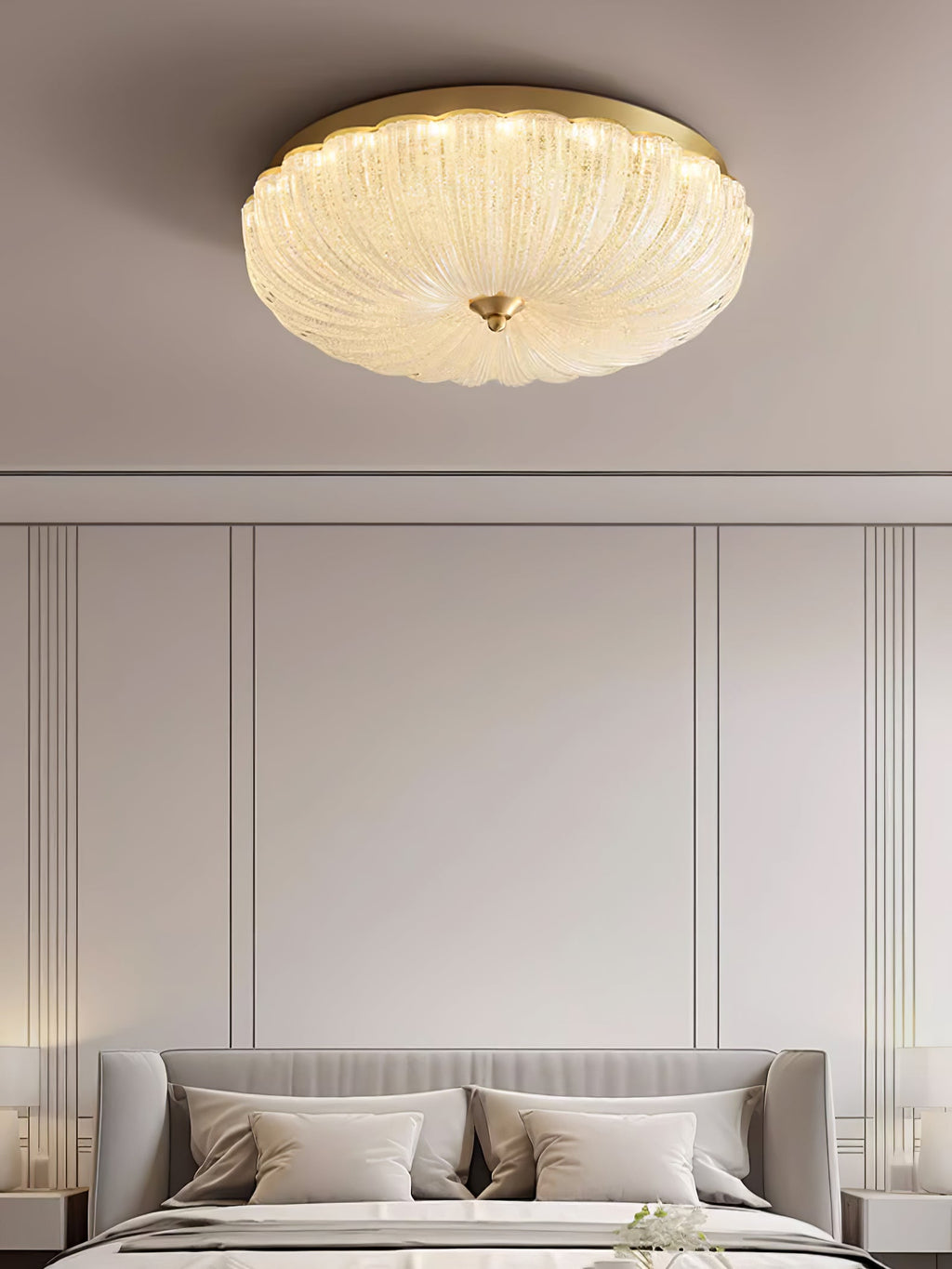 Clérachic ceiling light glowing above a cream panelled wall and a bed with a grey headboard and pale pillows.