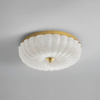 Unlit Clérachic ceiling light with a clear, ribbed glass shade, a gold backplate and a brass finial, on a plain grey backdrop.