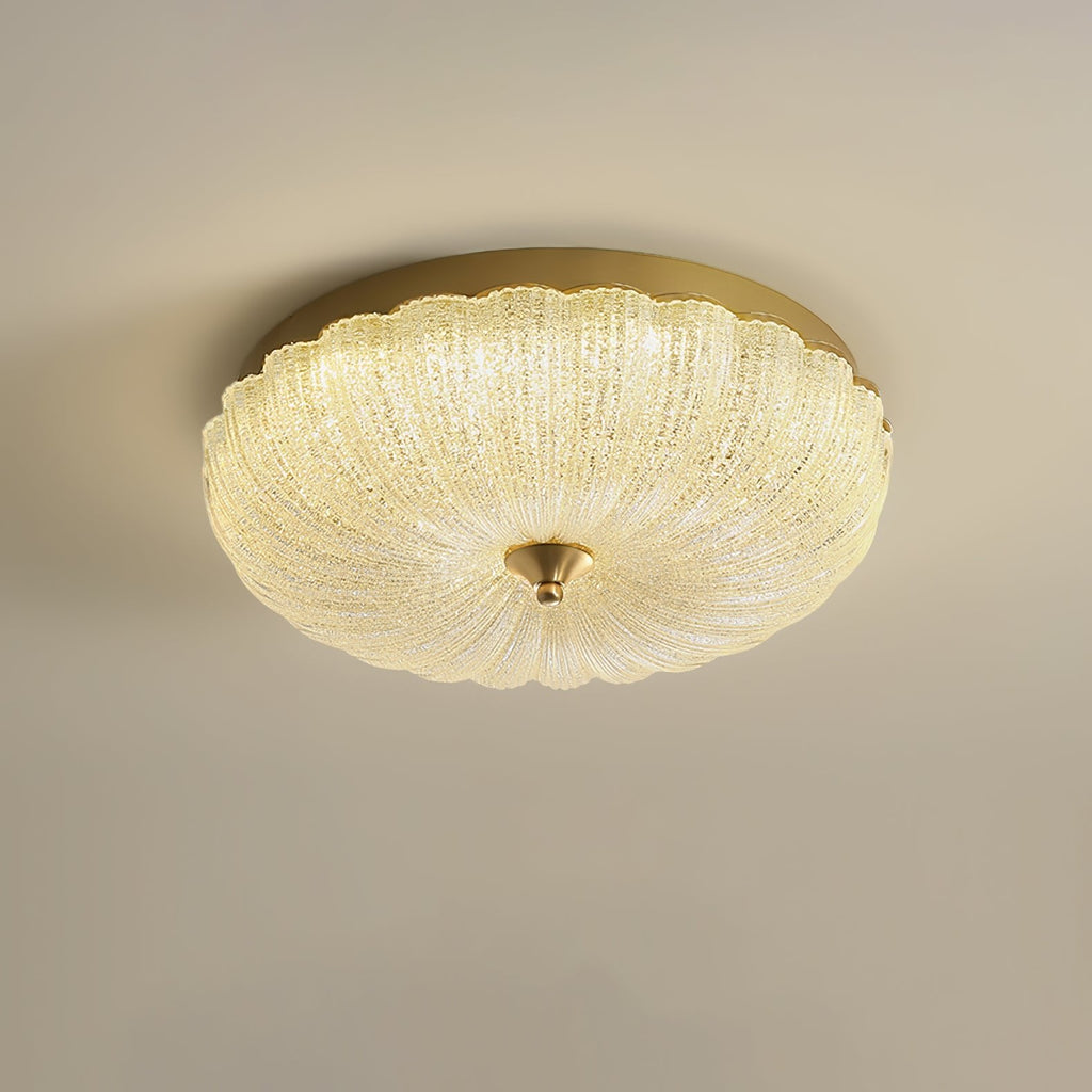 Warm-lit Clérachic ceiling light with a ribbed glass shade and a gold rim on a soft beige backdrop.