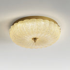 Lit Clérachic ceiling light with a golden-glowing ribbed glass shade, seen from slightly below on a pale grey backdrop.