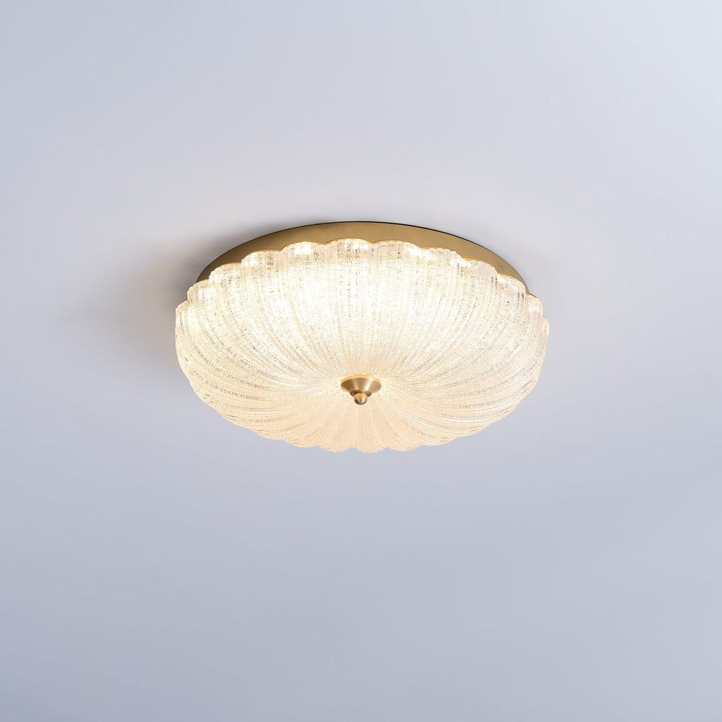 Clérachic flush ceiling light glowing warmly against a pale blue-grey ceiling, its scalloped glass shade ringed by gold.