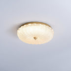 Clérachic flush ceiling light glowing warmly against a pale blue-grey ceiling, its scalloped glass shade ringed by gold.