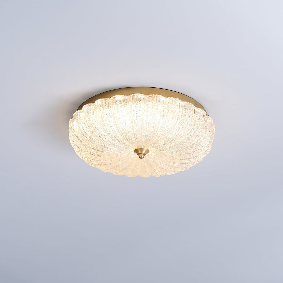 Clérachic flush ceiling light glowing warmly against a pale blue-grey ceiling, its scalloped glass shade ringed by gold.