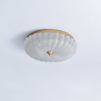 Unlit Clérachic ceiling light with a clear, textured glass shade and gold backplate, on a pale blue-grey ceiling.