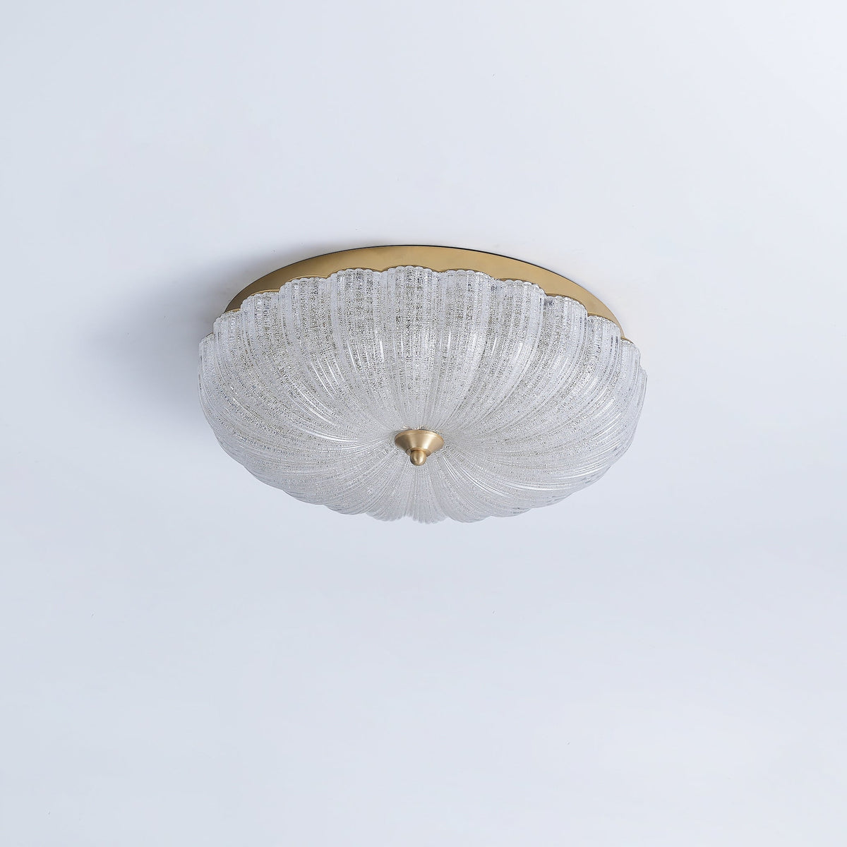 Unlit Clérachic ceiling light with a clear, textured glass shade and gold backplate, on a pale blue-grey ceiling.