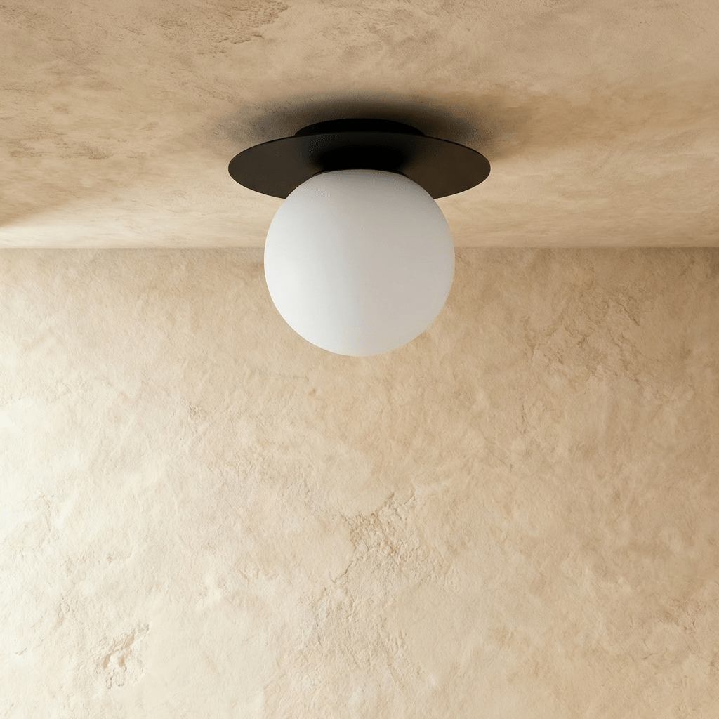A side view of the Clérachic ceiling light in black, its opal glass globe glowing softly on the ceiling.