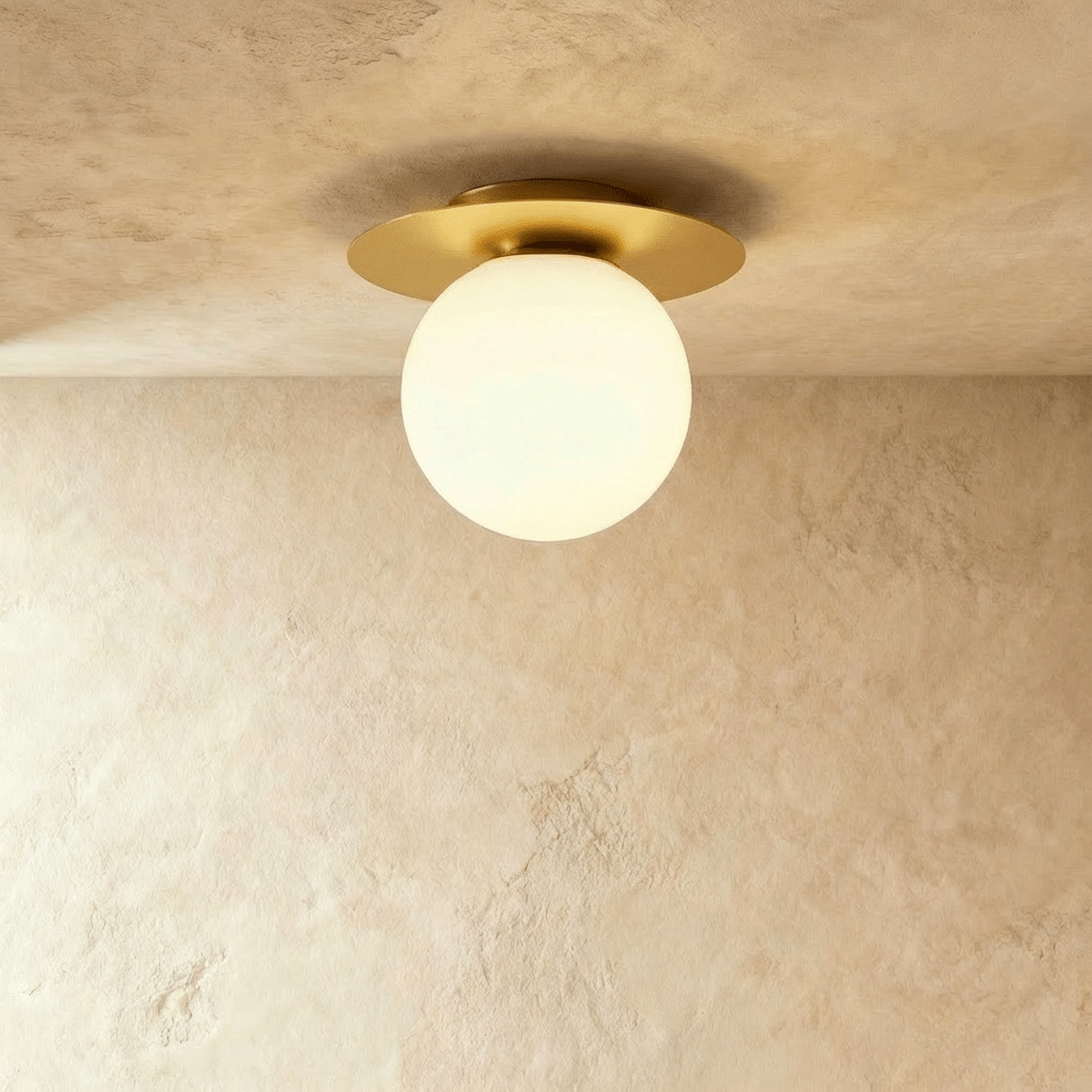Clérachic's ceiling light in gold, a round opal glass globe set beneath a brushed gold disc mount.
