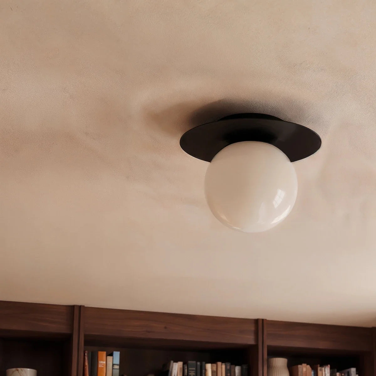 Clérachic's ceiling light in black, glowing warm above a built-in walnut bookshelf in a study.
