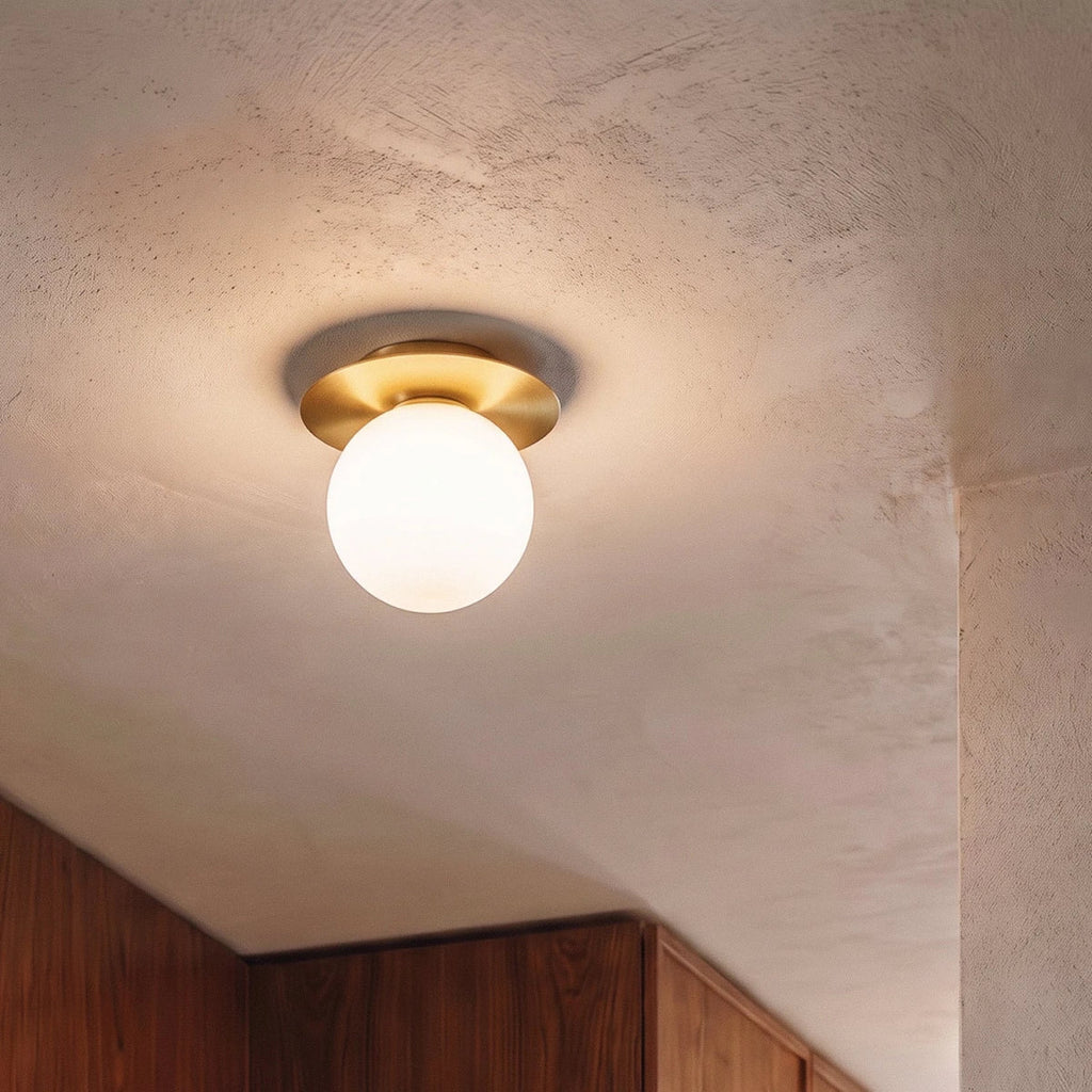 A close view of the Clérachic ceiling light in gold, glowing warm above wood cabinetry in a hallway.
