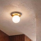 A close view of the Clérachic ceiling light in gold, glowing warm above wood cabinetry in a hallway.