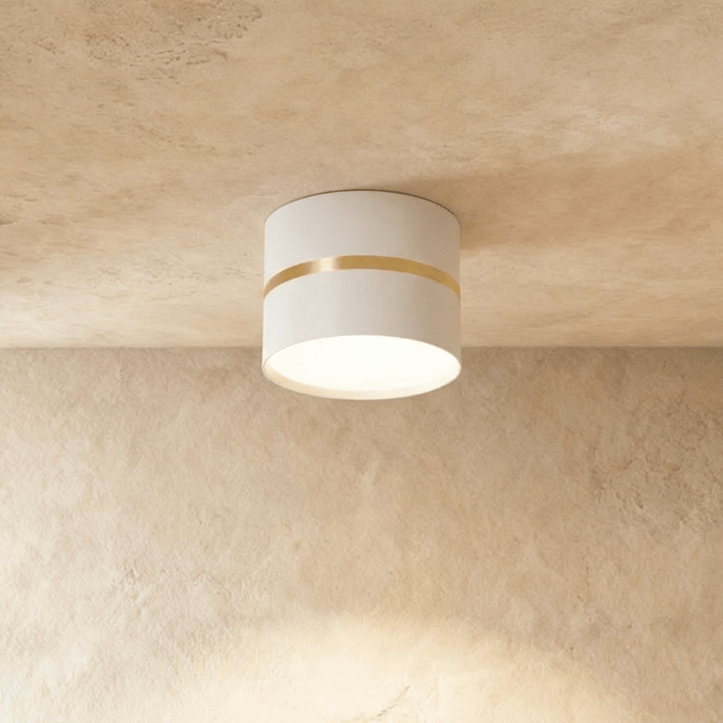 Clérachic white surface-mounted downlight with a slim brass ring accent, glowing on a plaster ceiling.
