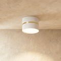 Clérachic white surface-mounted downlight with a slim brass ring accent, glowing on a plaster ceiling.