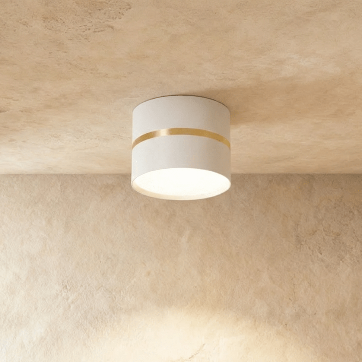 Clérachic white surface-mounted downlight with a slim brass ring accent, glowing on a plaster ceiling.