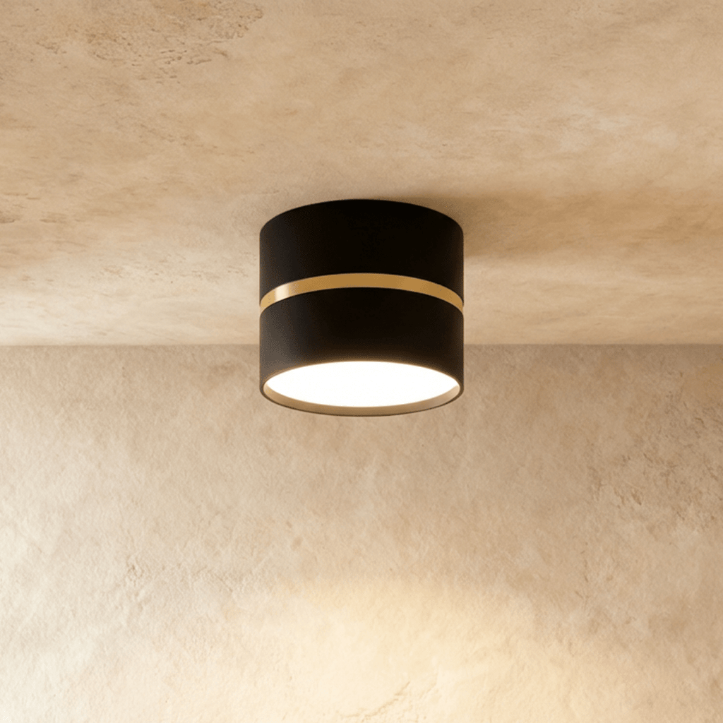 Clérachic black surface-mounted downlight with a slim brass ring accent, glowing on a plaster ceiling.