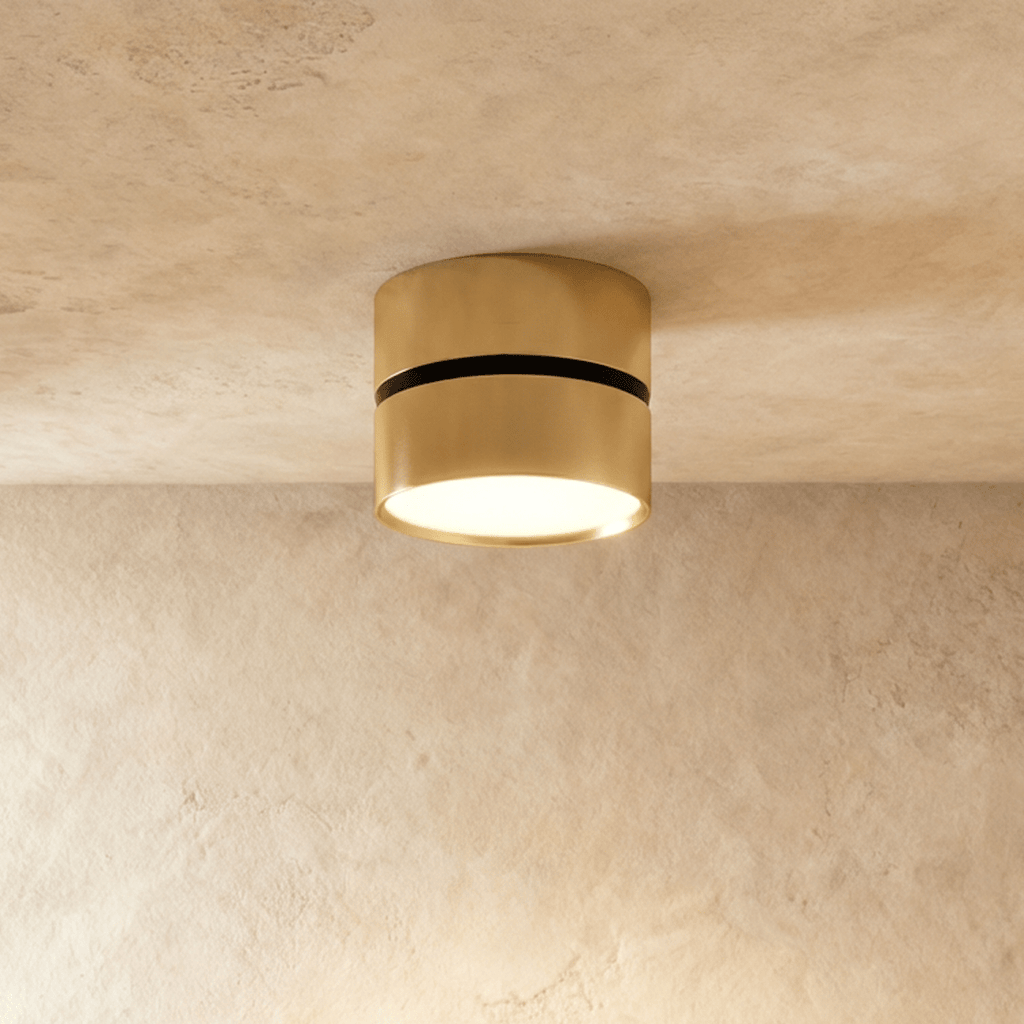 Clérachic brass surface-mounted downlight with a dark accent ring, glowing warm on a plaster ceiling.