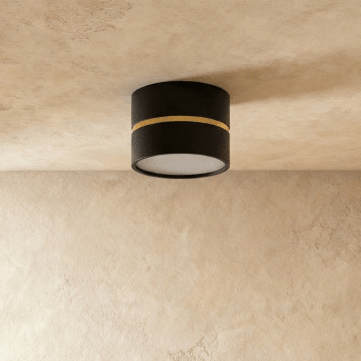 Clérachic black surface-mounted downlight with a thin brass ring, casting warm light onto a plaster ceiling.