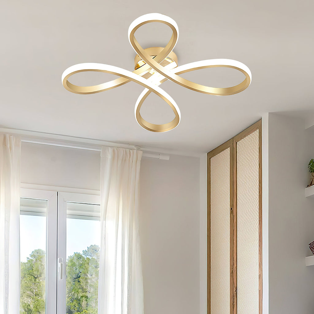 Large view of the gold four-loop Clérachic ceiling light from below, with tall windows and sheer curtains beside it.