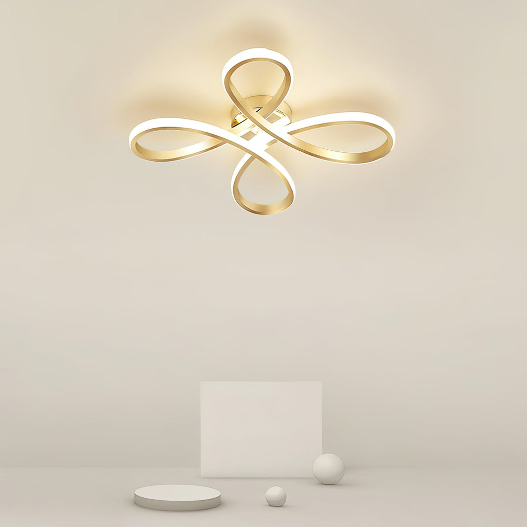 Close view of the lit Clérachic ceiling light on a cream ceiling, its four gold loops giving off a soft warm glow.