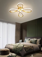 The gold four-loop Clérachic ceiling light above a bedroom with a dark green panelled wall, a grey bed and sheer curtains.
