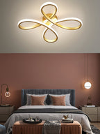 Close view of the Clérachic gold ceiling light above a bedroom with a terracotta wall, a blue-grey headboard and two small pendants.