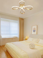 Gold Clérachic ceiling light above a bedroom with a pale bed, a knotted cushion, a window with blinds and gold curtains.