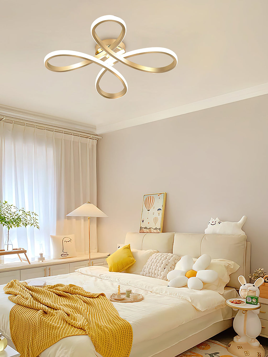 A Clérachic ceiling light above a bright bedroom with a white bed, a yellow throw, flower-shaped cushions and a table lamp.