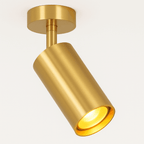 Clérachic gold ceiling spotlight lit, its gold cylinder tilted down with a warm glow inside the lamp opening.