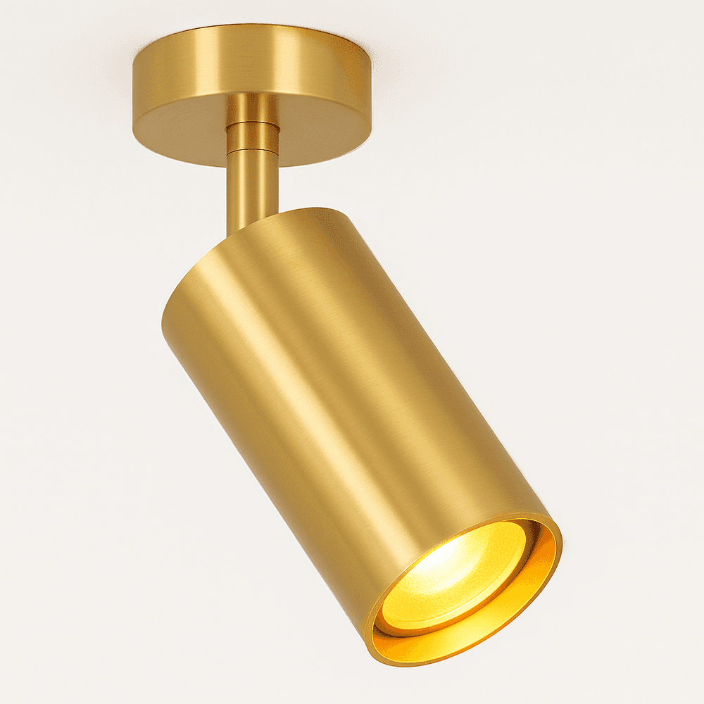 Clérachic gold ceiling spotlight lit, its gold cylinder tilted down with a warm glow inside the lamp opening.