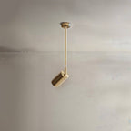 Clérachic gold ceiling spotlight on a longer rod with a small cylinder head, aimed down against a pale plaster wall.