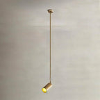 Clérachic gold ceiling spotlight on a very long thin gold rod, its cylinder head tilted and glowing against a stone-toned wall.