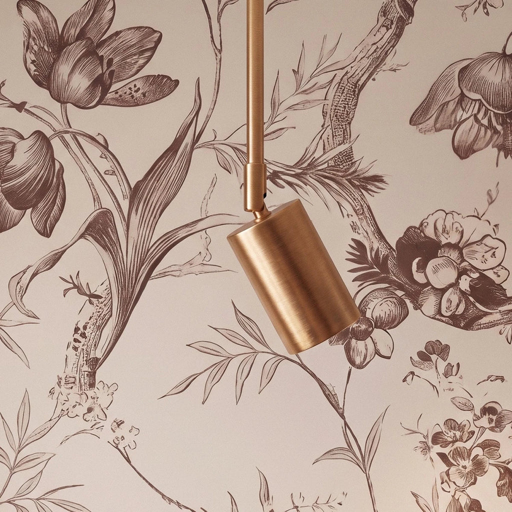 Close view of a Clérachic gold spotlight head on a slim gold rod, against toile floral wallpaper.