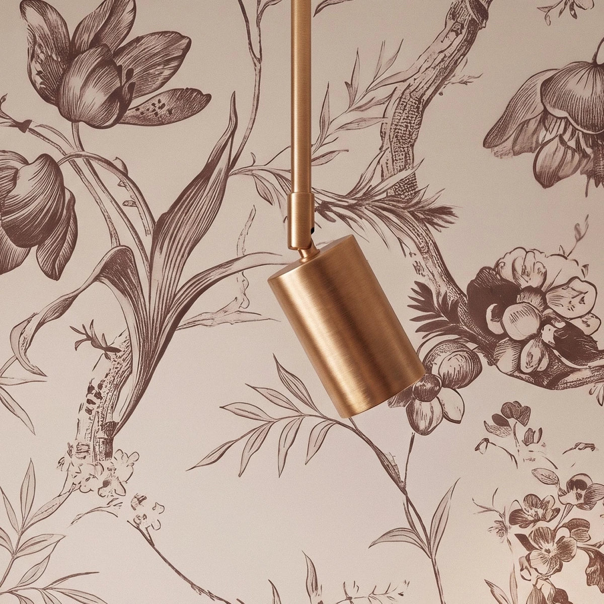 Close view of a Clérachic gold spotlight head on a slim gold rod, against toile floral wallpaper.
