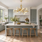 Gold branch arms and glowing blossoms on this Clérachic chandelier, hung above a blue-grey kitchen island with four wooden stools.