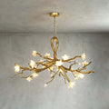 The Clérachic chandelier lit against a textured grey wall, showing its looped gold stem, branching arms and white ceramic blossoms.