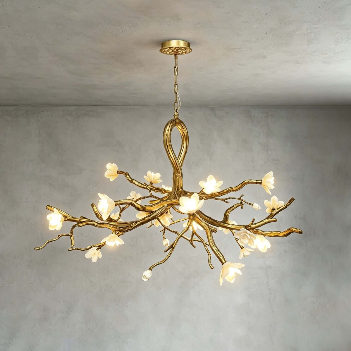 The Clérachic chandelier lit against a textured grey wall, showing its looped gold stem, branching arms and white ceramic blossoms.