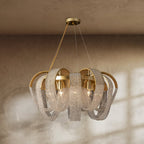 Clérachic gold chandelier hung with looping crystal bead chains over brass arches, lit with candle bulbs against a plaster wall.